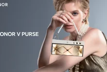 Woman holding a foldable phone that resembles a purse. The phone is Pink and has a gold chain strap. The text "HONOR V PURSE" is displayed on the phone.