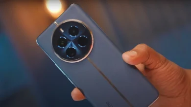 Close-up of a person holding a black Realme 12 Pro Plus 5G smartphone. The phone has a large screen and a triple-lens rear camera.